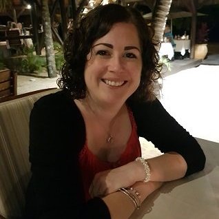 Smiling woman with shoulder length dark curly hair, wearing a red top and black cardigan.